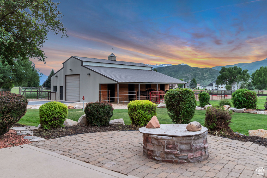Back of house at dusk with a mountain view, an exterior structure, an outdoor structure, a fire pit, and a metal roof