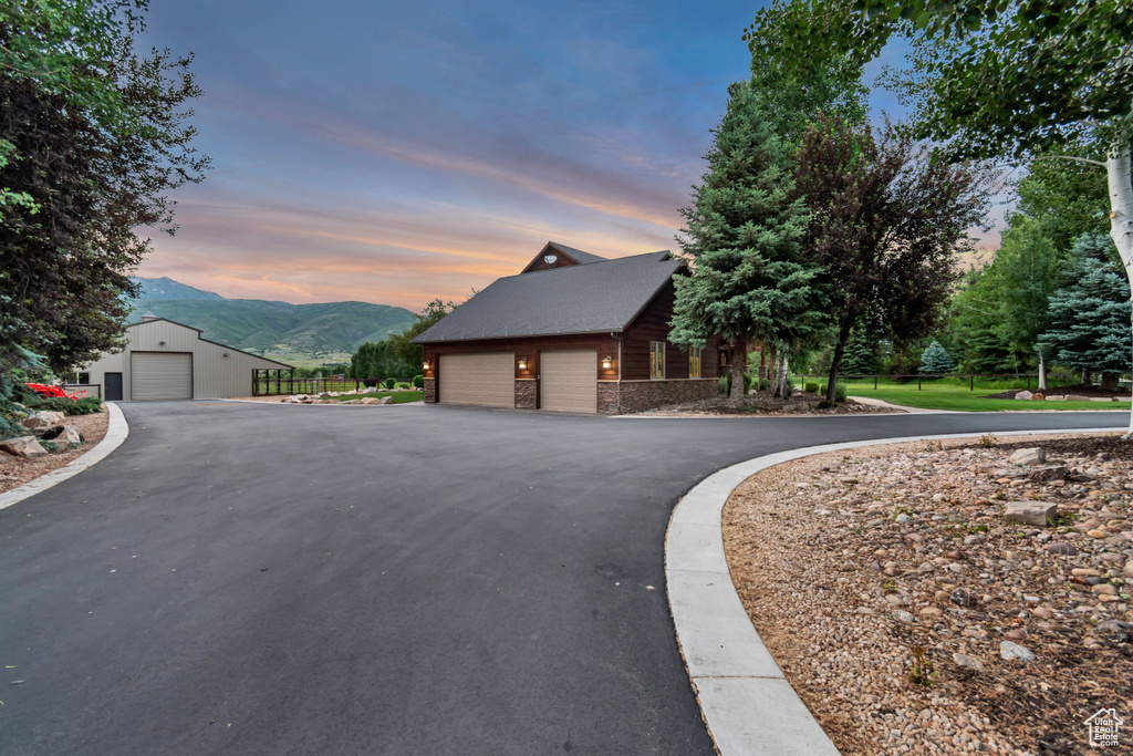 Property exterior at dusk with a mountain view, an outdoor structure, stone siding, and a detached garage