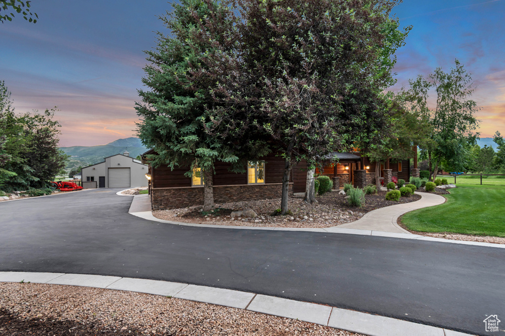 View of front of home featuring stone siding, a detached garage, an outdoor structure, a yard, and a mountain view