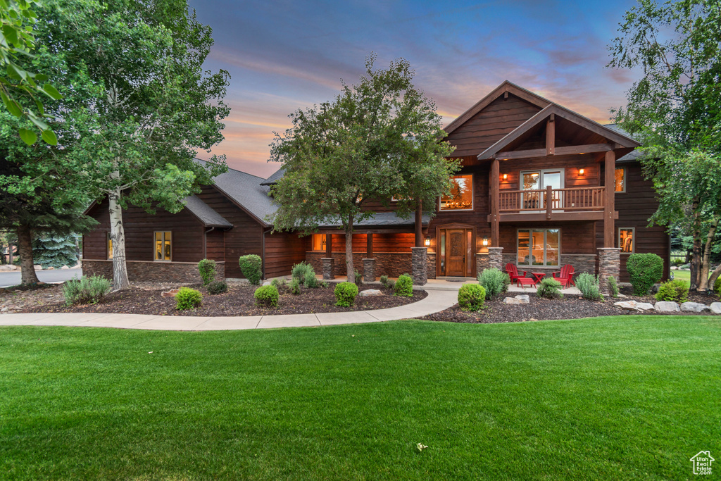 Log-style house with stone siding, a balcony, and a lawn