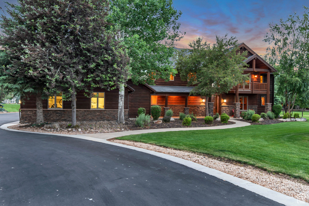 View of front of property with stone siding, a lawn, a balcony, and driveway