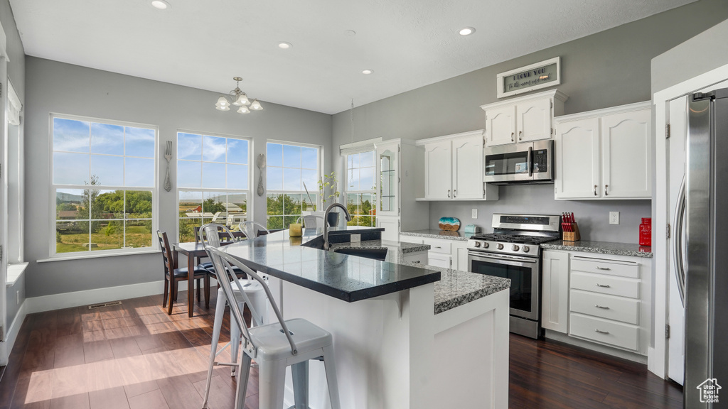 Kitchen featuring appliances with stainless steel finishes, recessed lighting, white cabinetry, a kitchen bar, and a center island with sink