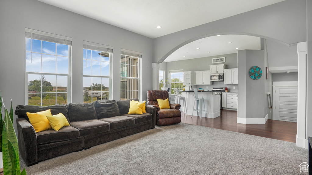 Living area with dark colored carpet, arched walkways, recessed lighting, and dark wood-type flooring