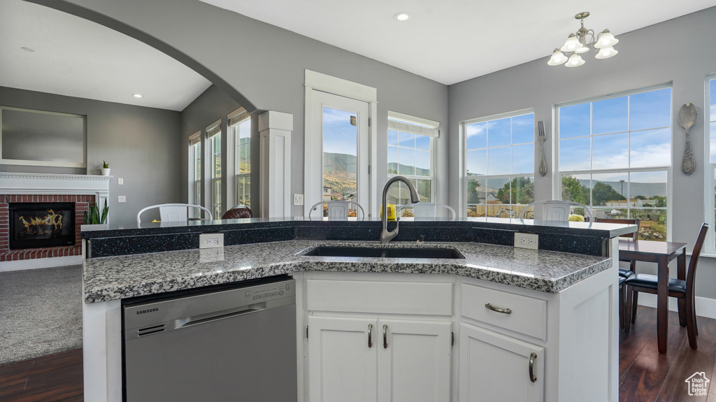 Kitchen featuring dishwasher, arched walkways, dark wood-style flooring, white cabinets, and a chandelier