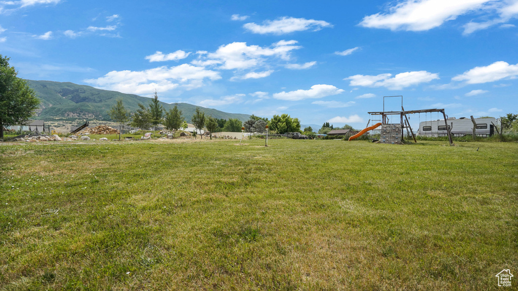 View of grassy yard with a playground and a mountain view