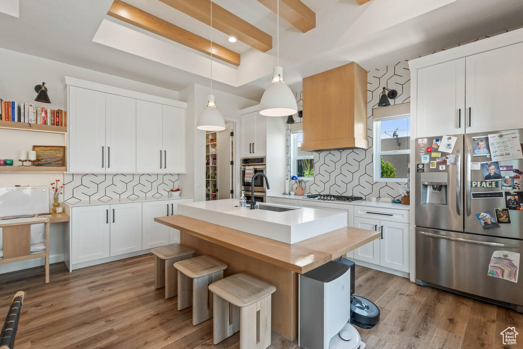 Kitchen featuring appliances with stainless steel finishes, light wood-type flooring, tasteful backsplash, light countertops, and beam ceiling
