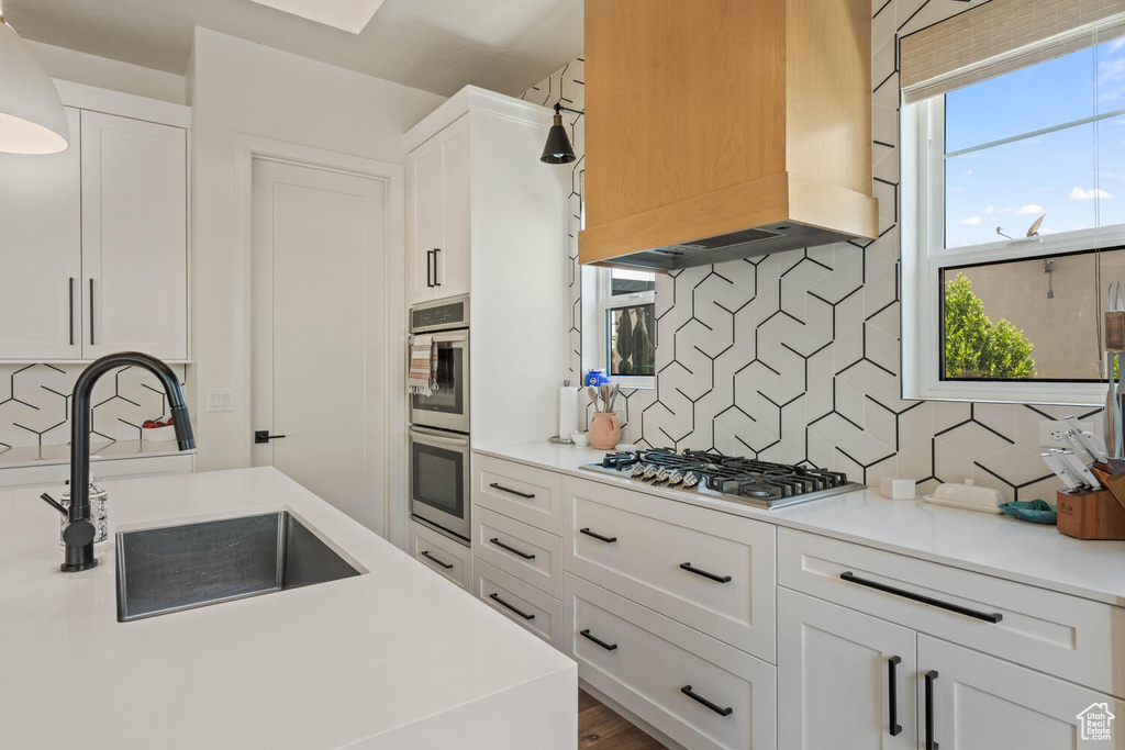 Kitchen featuring custom range hood, appliances with stainless steel finishes, decorative backsplash, and white cabinetry