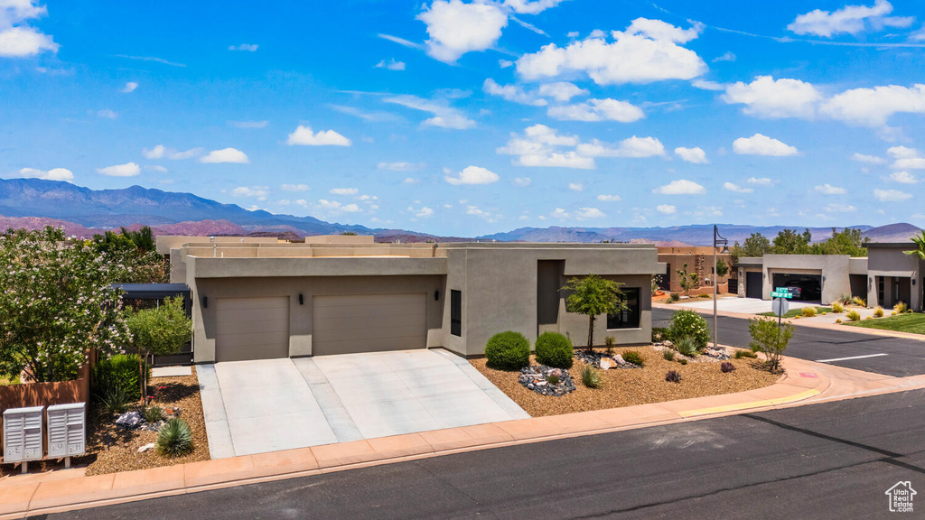 Pueblo-style house with a mountain view, a garage, stucco siding, and concrete driveway