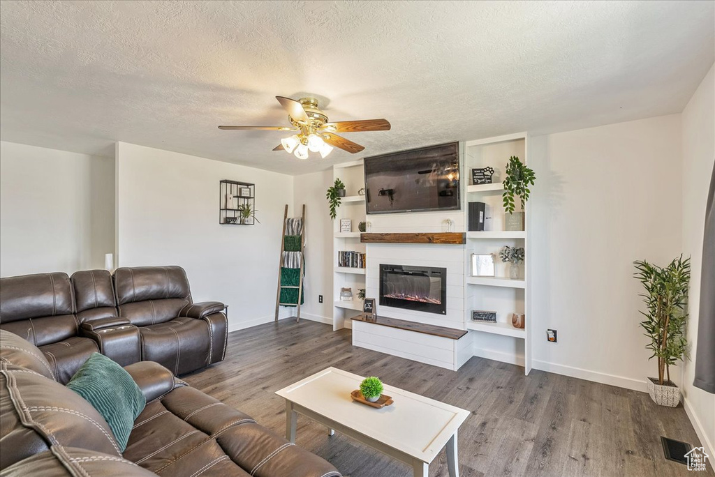 Living room featuring wood finished floors, a ceiling fan, a textured ceiling, and a fireplace
