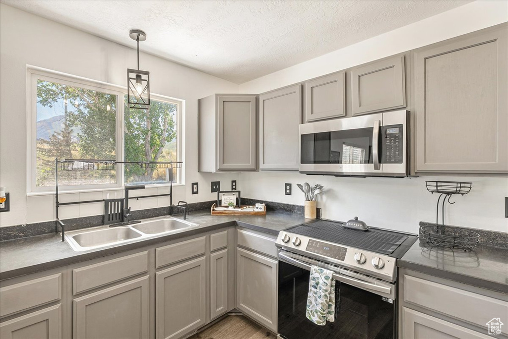 Kitchen with stainless steel appliances, dark countertops, gray cabinets, decorative light fixtures, and a textured ceiling