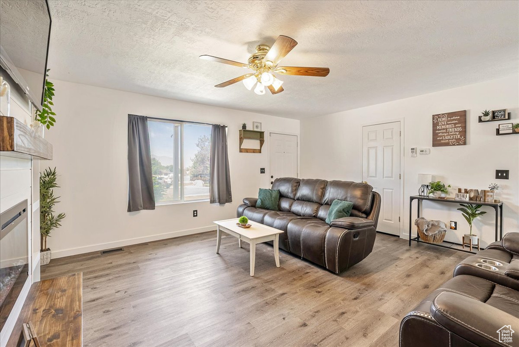 Living area featuring ceiling fan, a textured ceiling, light wood-style floors, and a glass covered fireplace