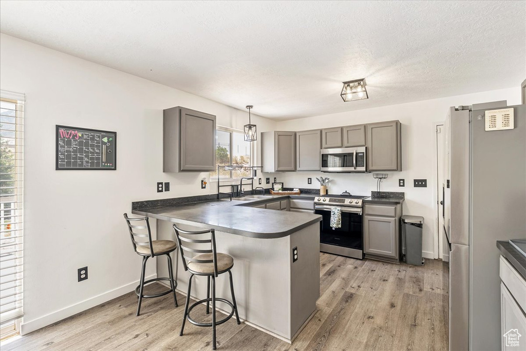 Kitchen featuring appliances with stainless steel finishes, a peninsula, gray cabinets, dark countertops, and a breakfast bar area