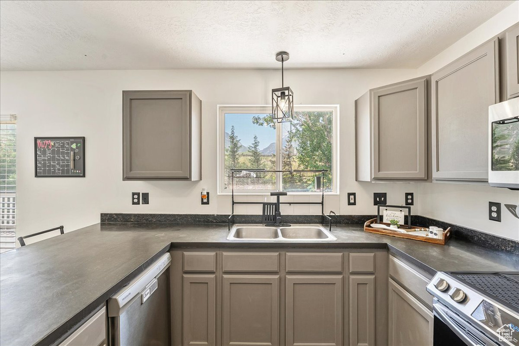 Kitchen featuring stainless steel appliances, gray cabinetry, dark countertops, plenty of natural light, and a textured ceiling