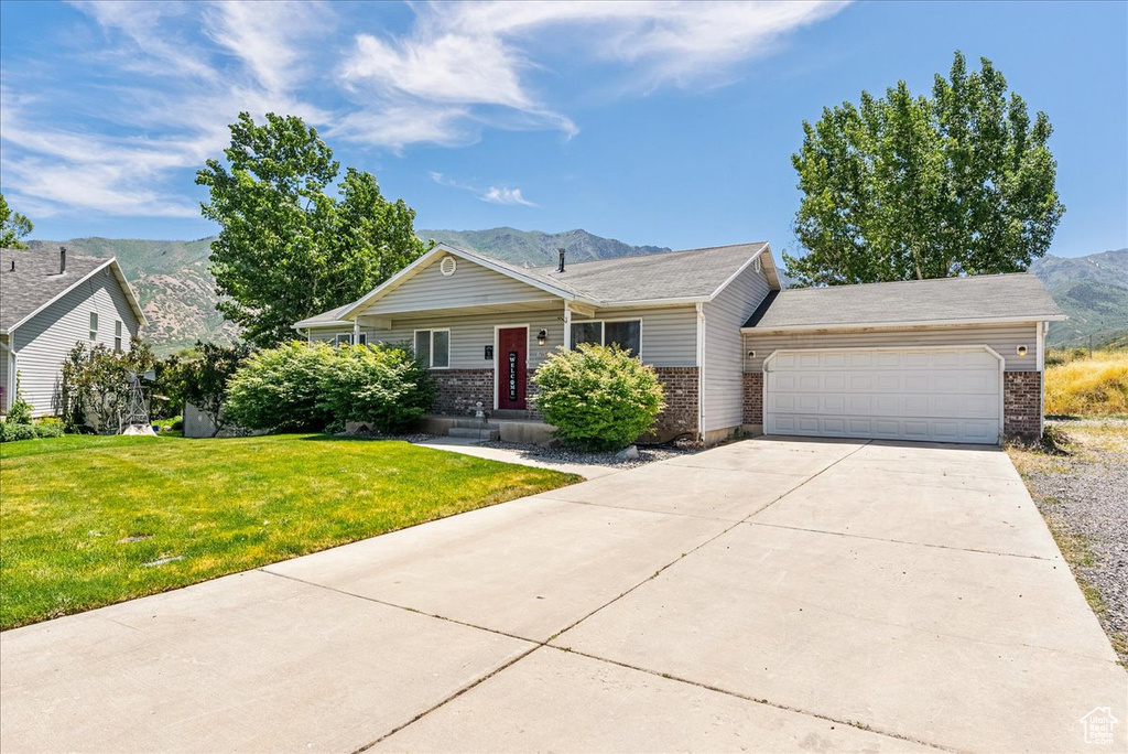 Single story home featuring brick siding, a mountain view, an attached garage, a front yard, and concrete driveway