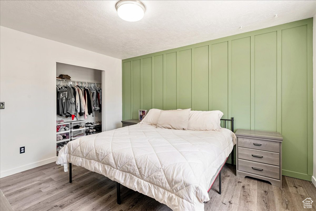 Bedroom with light wood-style floors, a closet, a decorative wall, and a textured ceiling