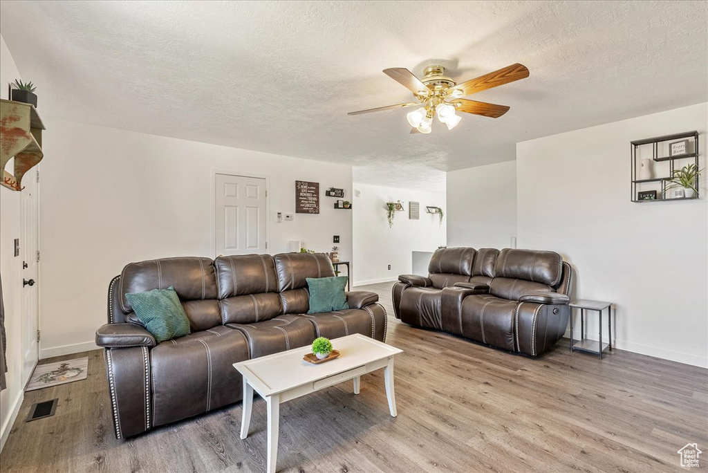 Living room with ceiling fan, light wood-style flooring, and a textured ceiling