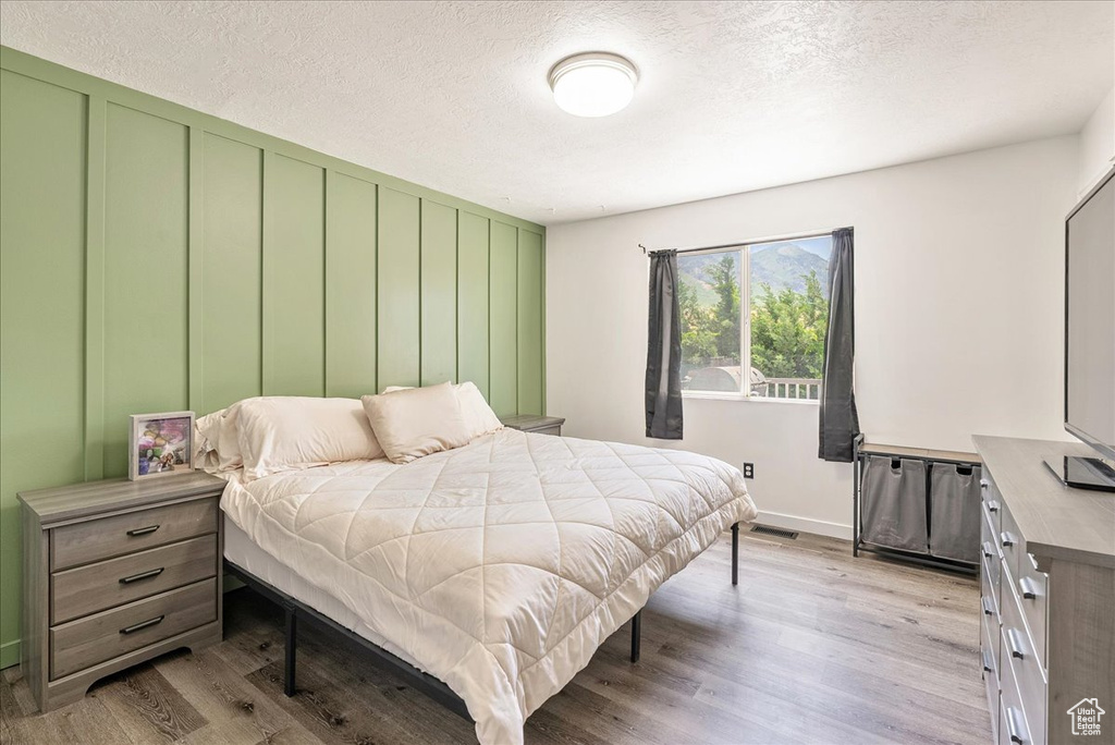 Bedroom with light wood-style floors, a textured ceiling, and a decorative wall