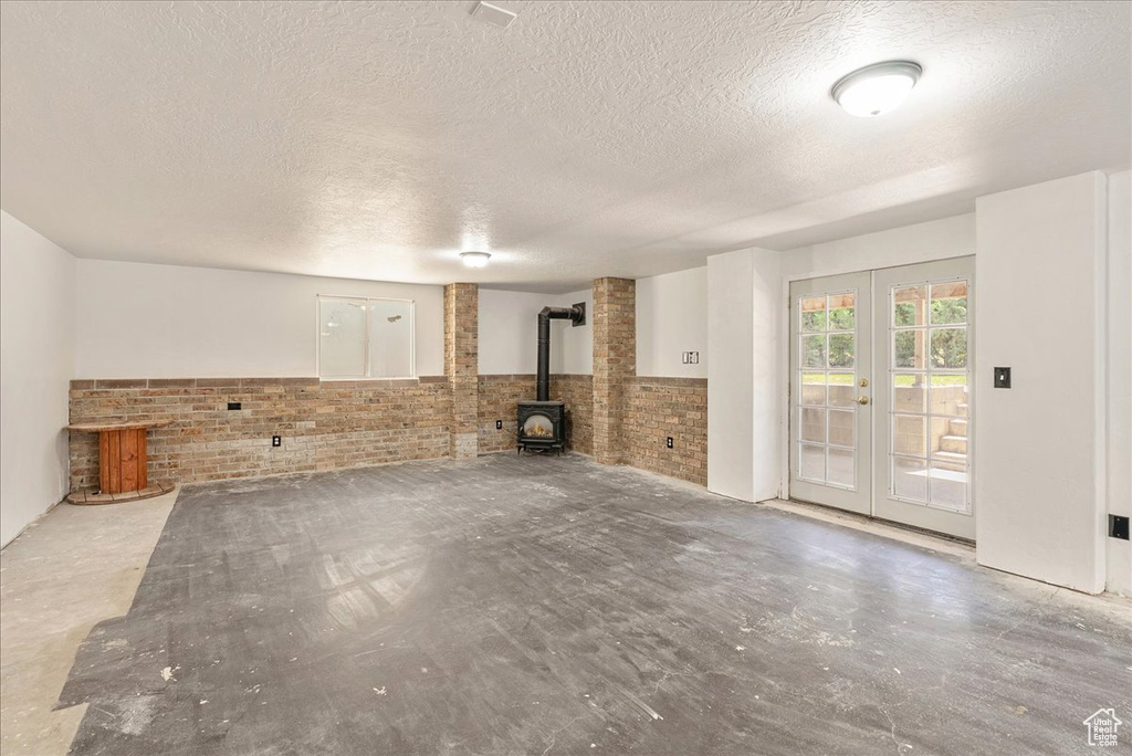 Unfurnished living room featuring brick wall, a wood stove, french doors, a textured ceiling, and a wainscoted wall