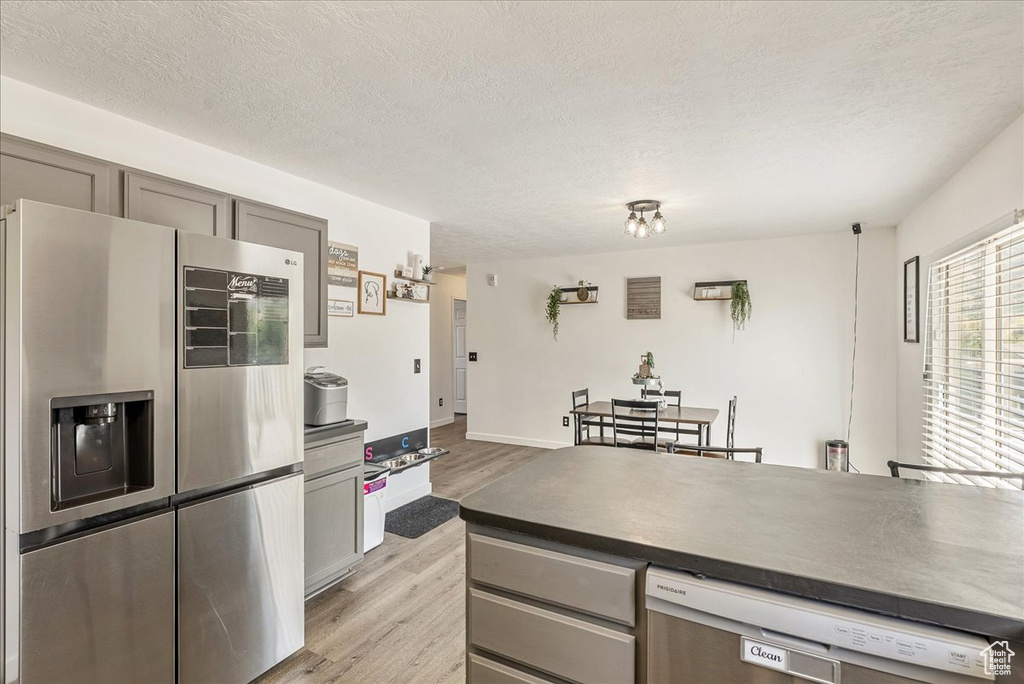 Kitchen featuring appliances with stainless steel finishes, light wood-style flooring, gray cabinetry, a textured ceiling, and dark countertops