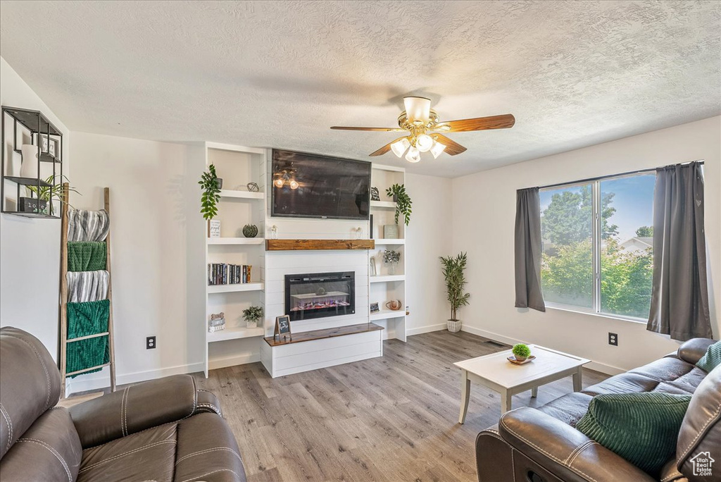 Living area with ceiling fan, wood finished floors, a textured ceiling, and a fireplace