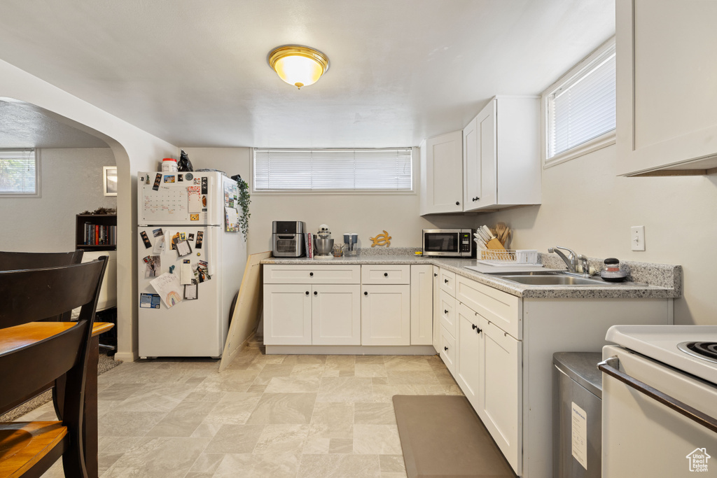 Kitchen with white appliances, white cabinetry, arched walkways, and light countertops