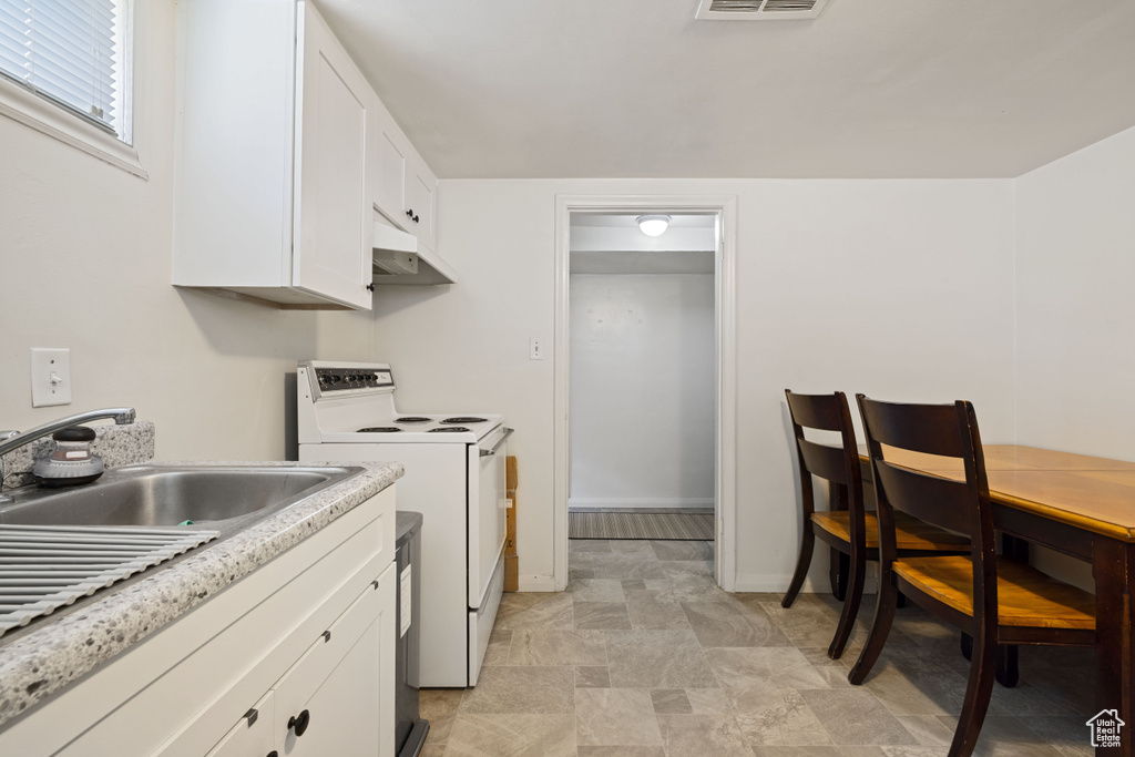 Kitchen with white electric stove, under cabinet range hood, white cabinetry, light countertops, and stone finish floors