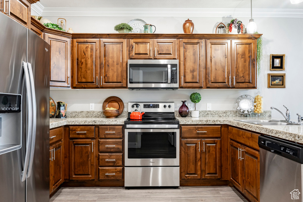 Kitchen featuring stainless steel appliances, ornamental molding, light wood-style flooring, decorative light fixtures, and light stone countertops