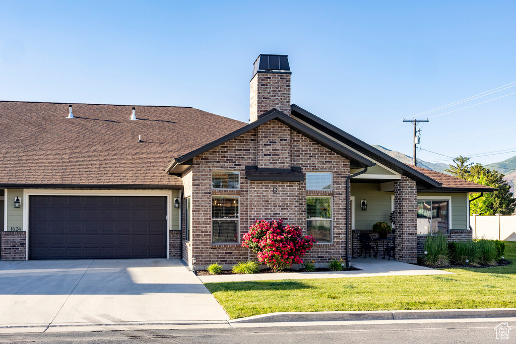 View of front of home featuring brick siding, a chimney, driveway, and roof with shingles