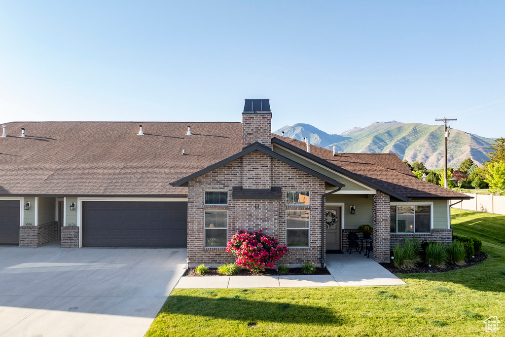 View of front of house with brick siding, an attached garage, a front lawn, a mountain view, and concrete driveway