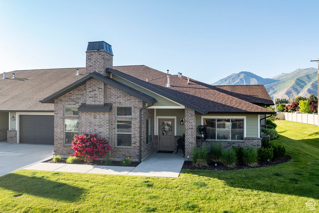 View of front facade with brick siding, an attached garage, concrete driveway, roof with shingles, and a mountain view