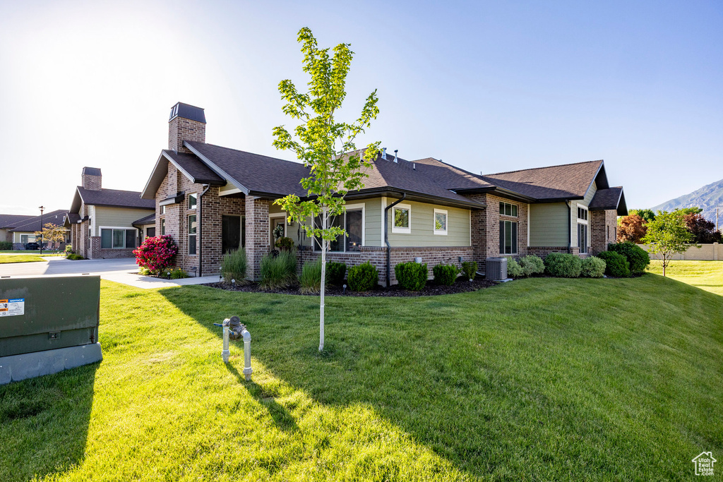 View of front of house featuring brick siding, a front lawn, a shingled roof, and a chimney