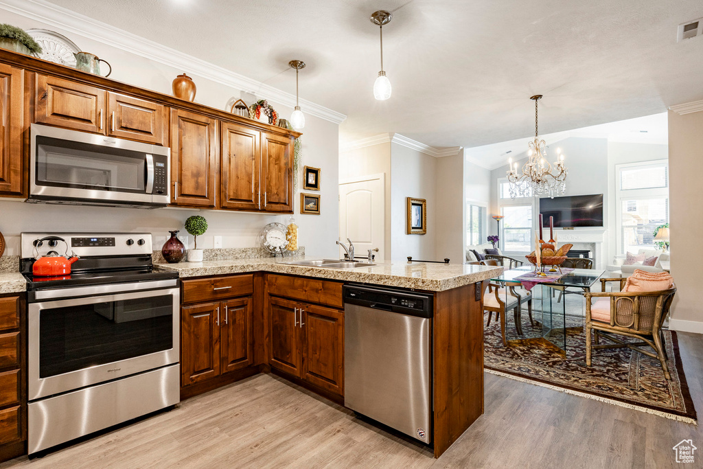 Kitchen featuring stainless steel appliances, light wood-style floors, a peninsula, crown molding, and a chandelier