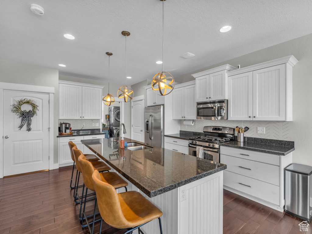 Kitchen featuring stainless steel appliances, stacked washer / drying machine, dark wood finished floors, decorative backsplash, and recessed lighting