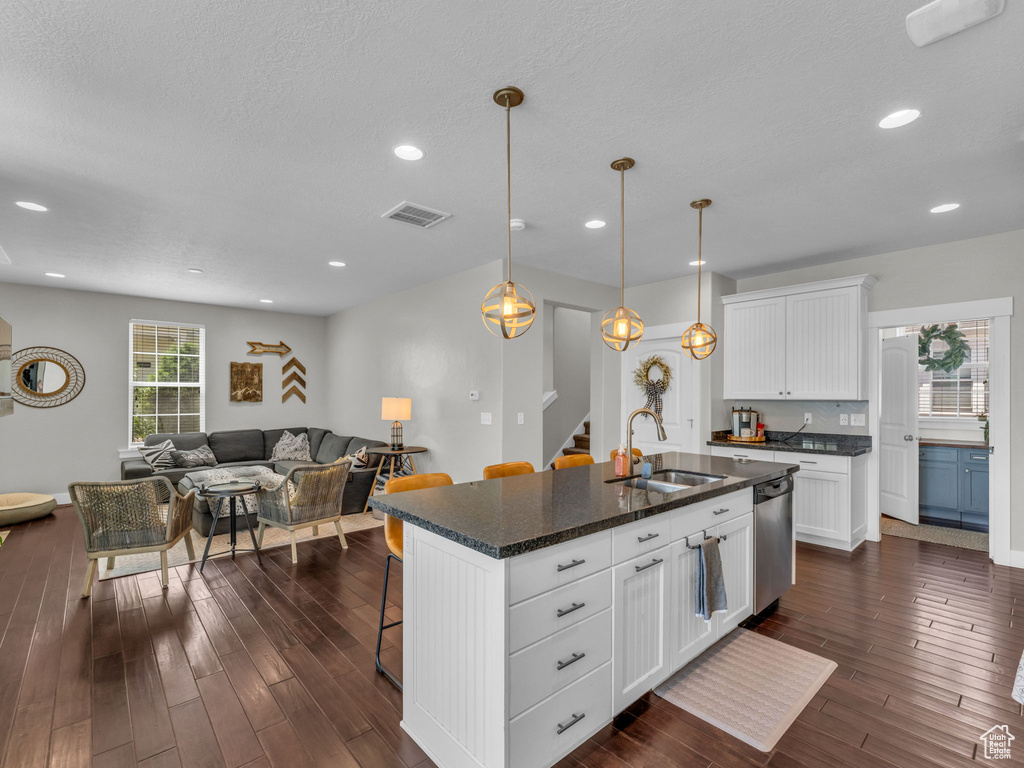 Kitchen with stainless steel dishwasher, a breakfast bar area, dark wood-style floors, open floor plan, and white cabinetry