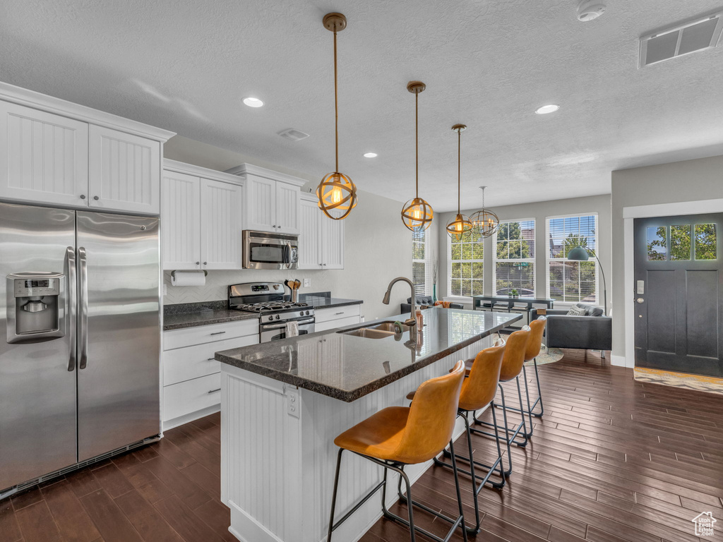 Kitchen featuring appliances with stainless steel finishes, dark wood-style flooring, a textured ceiling, white cabinetry, and recessed lighting