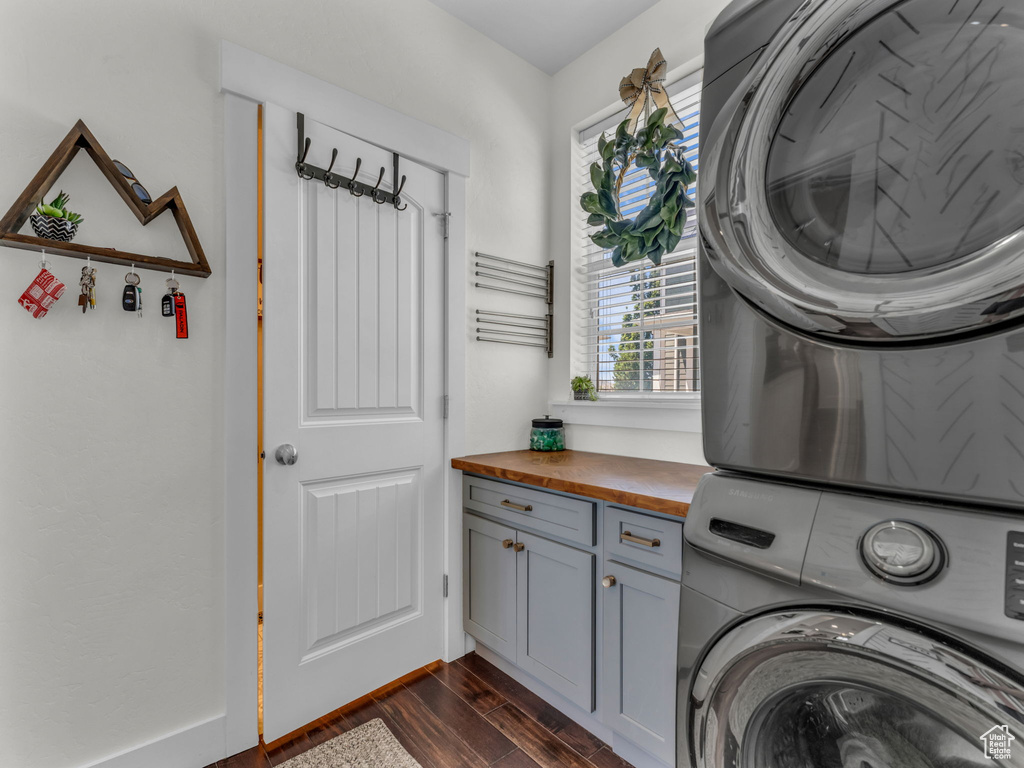 Laundry room featuring stacked washer and clothes dryer, cabinet space, and dark wood-style flooring