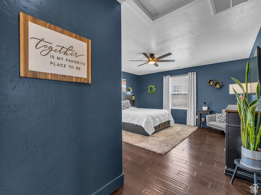 Bedroom with a textured ceiling, wood finished floors, ceiling fan, and a textured wall