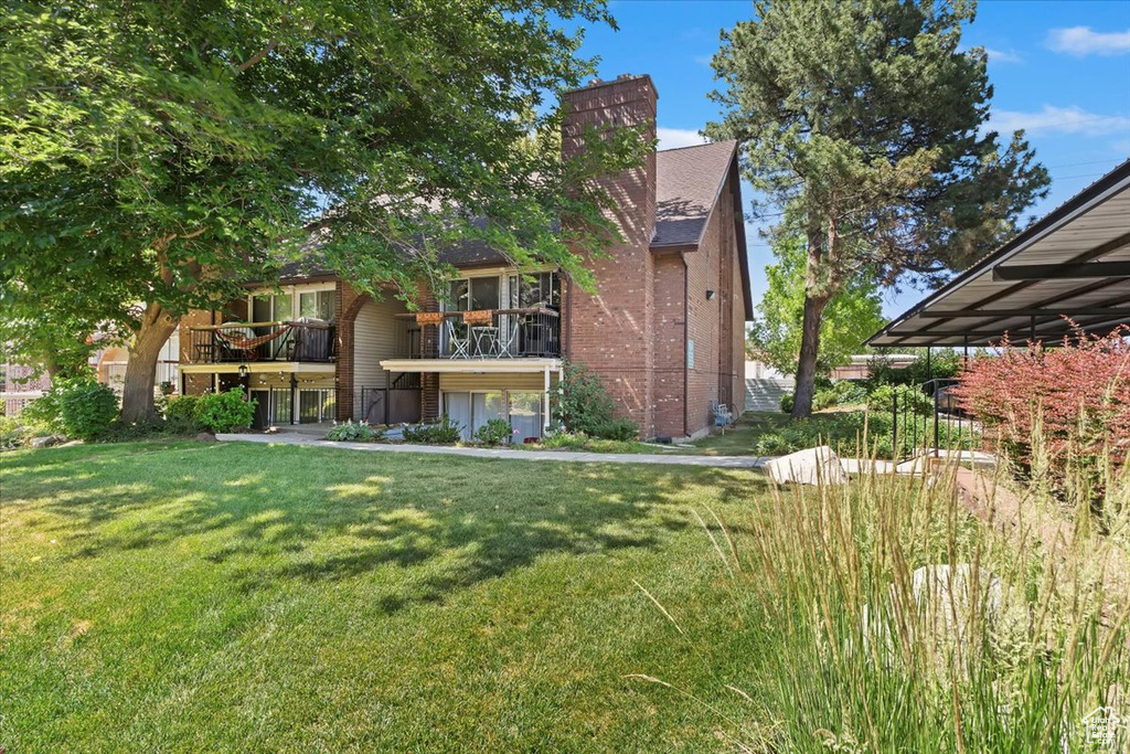 Exterior space with a lawn, a balcony, a chimney, and brick siding