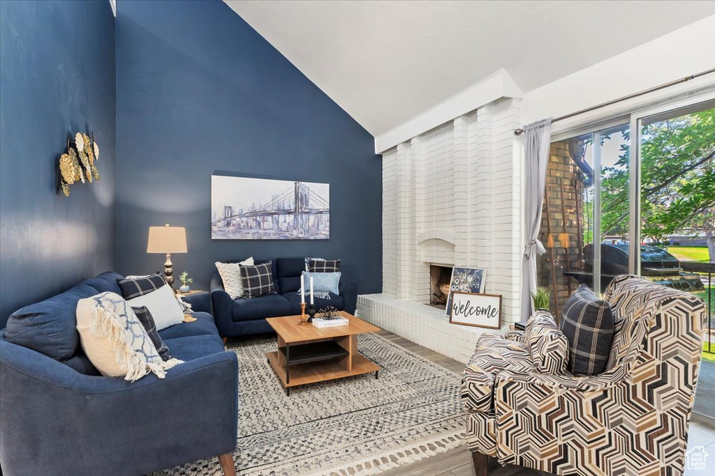 Living room with wood finished floors, a brick fireplace, and high vaulted ceiling