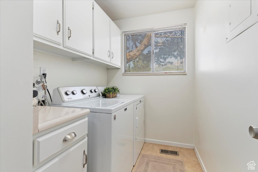 Laundry room featuring washing machine and clothes dryer, cabinet space, and light tile patterned flooring