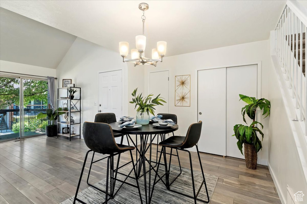 Dining area with a chandelier, wood finished floors, lofted ceiling, and stairway