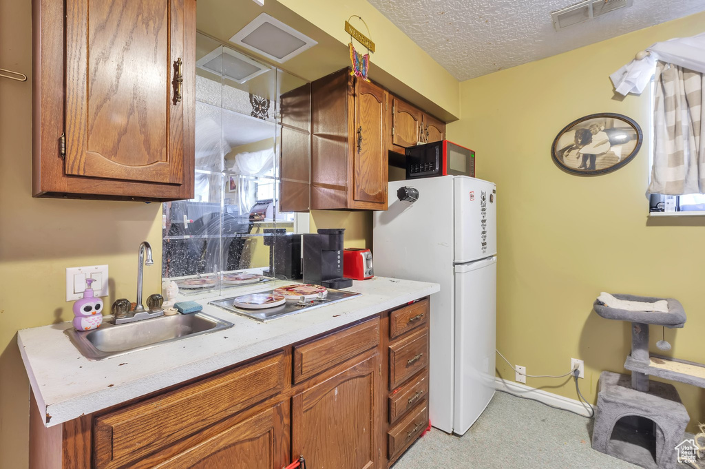 Kitchen with freestanding refrigerator, black microwave, brown cabinets, light countertops, and a textured ceiling