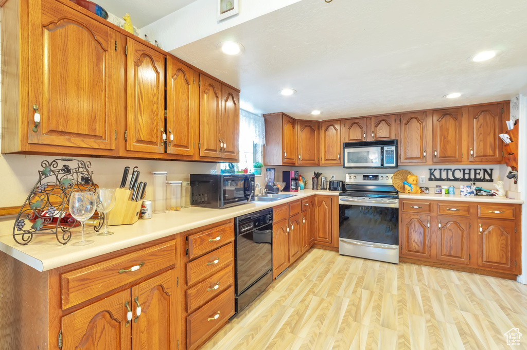 Kitchen with black appliances, brown cabinetry, light wood-style flooring, light countertops, and recessed lighting