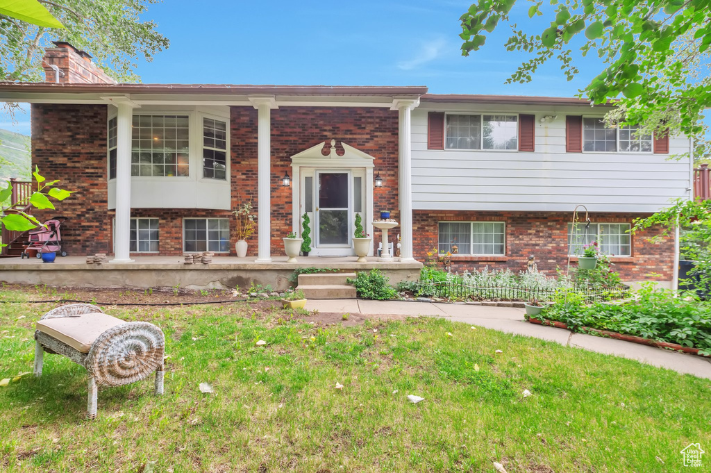 Split foyer home featuring brick siding, covered porch, a chimney, and a front lawn