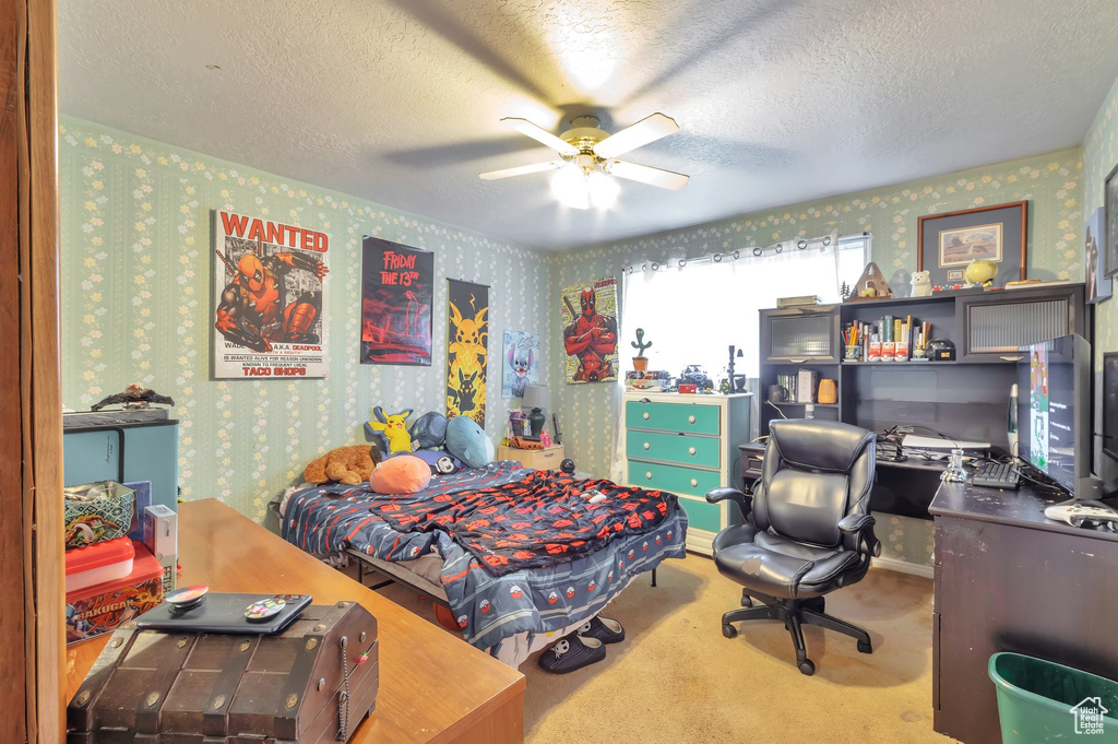 Carpeted bedroom featuring wallpapered walls, a textured ceiling, a desk, and ceiling fan