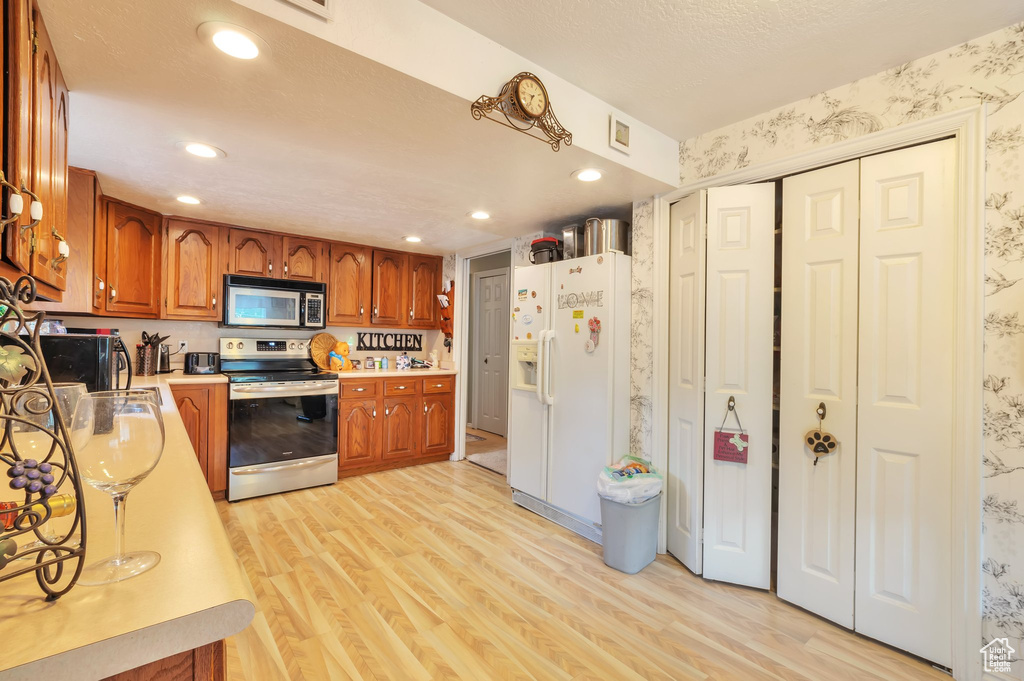 Kitchen featuring stainless steel appliances, wallpapered walls, light wood-type flooring, light countertops, and brown cabinetry