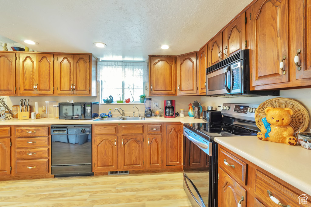 Kitchen featuring black appliances, brown cabinets, recessed lighting, light countertops, and light wood-style floors