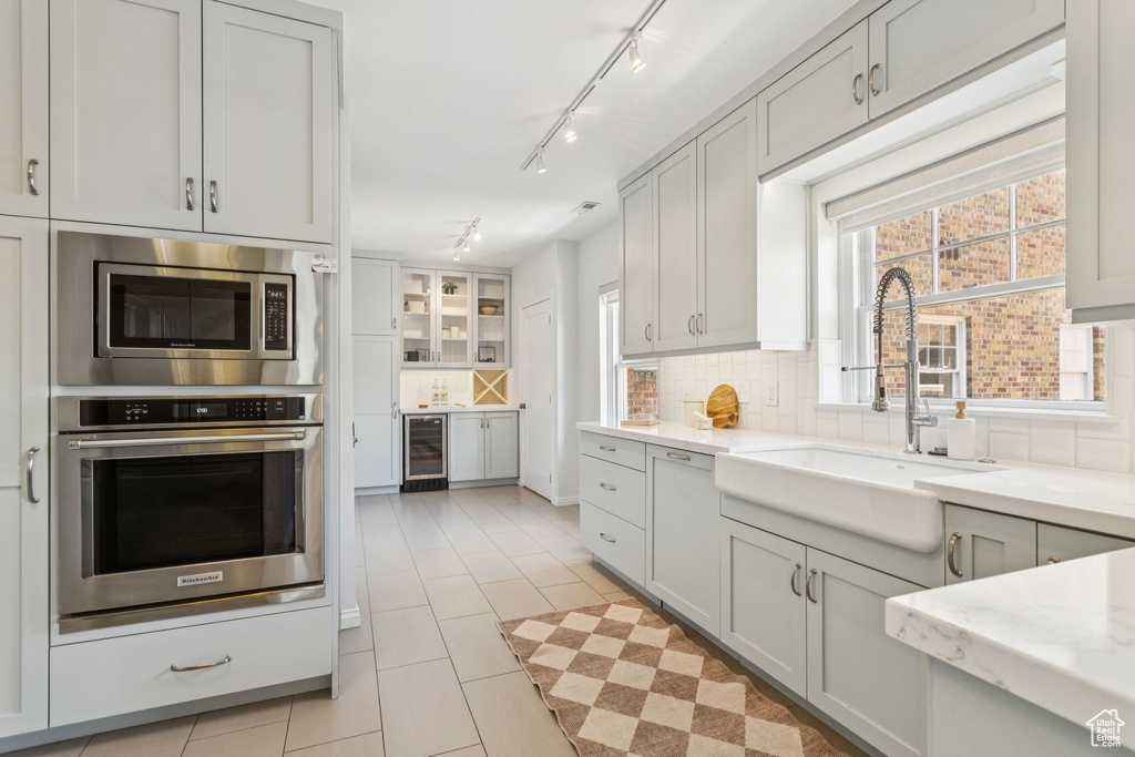Kitchen with stainless steel appliances, wine cooler, track lighting, tasteful backsplash, and light tile patterned flooring
