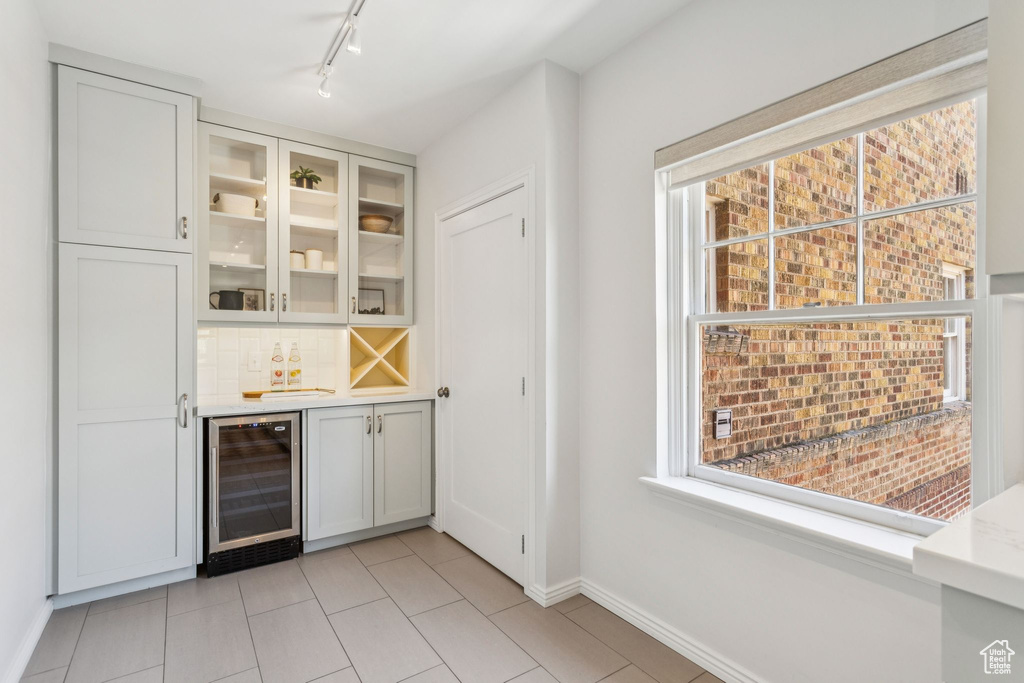 Indoor dry bar featuring beverage cooler, rail lighting, light tile patterned floors, and tasteful backsplash