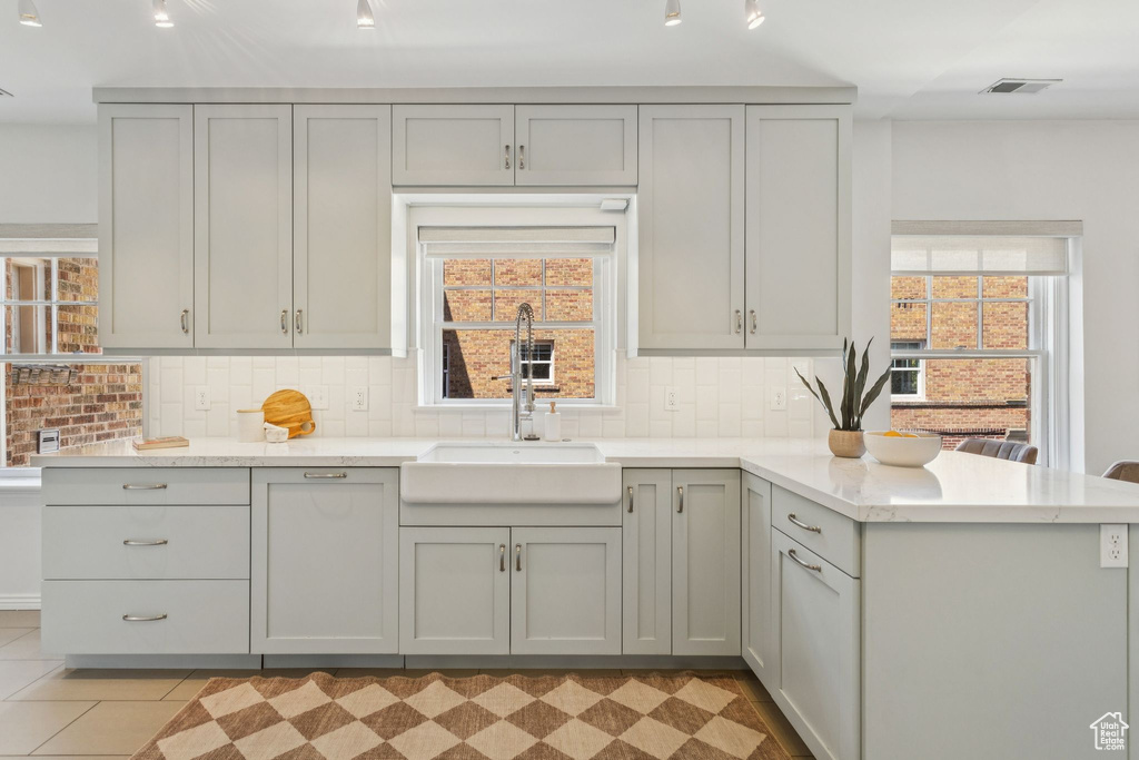 Kitchen with a peninsula, backsplash, light stone counters, gray cabinetry, and light floors